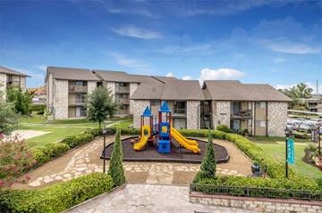 San Antonio apartment for rent - A playground with a slide and swings is surrounded by a well-manicured lawn and apartment buildings.