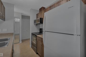 Fort Saskatchewan apartment for rent - A white refrigerator stands in a kitchen with wooden cabinets and a stainless steel sink.