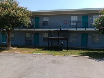 Corpus Christi apartment for rent - A small tree is in front of a grey building with blue doors.
