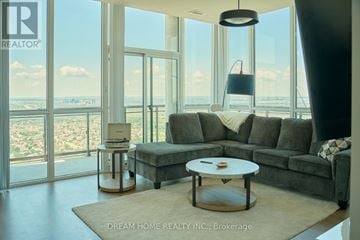 Mississauga (City Centre) condo for rent - A modern living room with a grey sofa and a coffee table in front of a large window.
