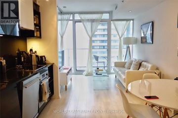 Toronto (Waterfront Communities) condo for rent - A modern kitchen with a dining table and chairs in the foreground and a living room with a couch and a large window in the background.