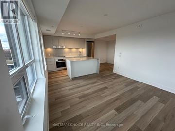 Markham (Unionville) condo for rent - A spacious room with wooden flooring and a kitchen area in the background.