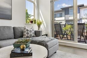 Surrey townhouse for rent - A living room with a grey couch, a small table with a plant and a book on it, and a view of a balcony with chairs.