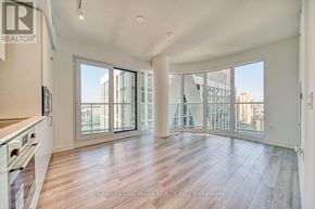 Toronto (Kensington-Chinatown) condo for rent - A spacious living room with a kitchen area to the left and a view of the city through the large windows.