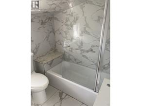 Vancouver apartment for rent - A white toilet sits next to a marble tiled shower.