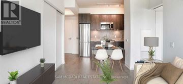 Toronto (Niagara) condo for rent - A living room with a couch, a dining table, and a television mounted on the wall.