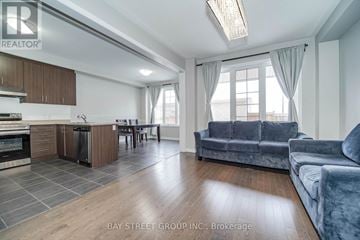 Markham (Cornell) apartment for rent - A spacious living room with a grey sofa and a kitchen area with wooden cabinets.