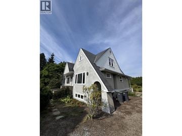 Vancouver apartment for rent - A house with a grey roof and white walls is surrounded by a dirt area and trees.