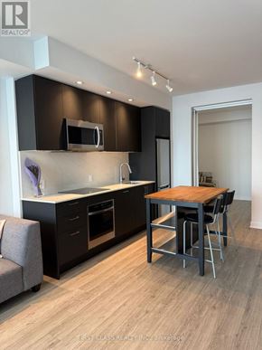 Toronto (South Parkdale) condo for rent - A modern kitchen with dark brown cabinets and a wooden table.