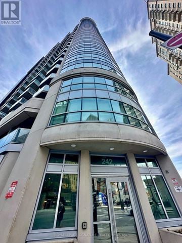 Ottawa condo for rent - A tall building with a curved glass facade and a sign that reads "242" is seen from the street level.