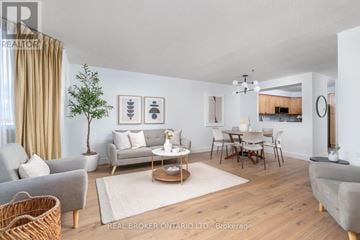 Toronto (Long Branch) condo for rent - A well-lit living room with a grey sofa, a wooden coffee table, and a dining table with chairs.