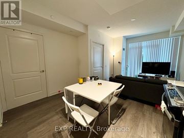 Toronto (Willowdale East) condo for rent - A living room with a white table and chairs, a black couch, and a television.