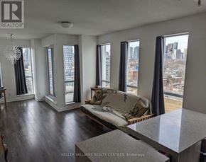 Toronto (Regent Park) condo for rent - A living room with a couch and a table in front of a window with a city view.