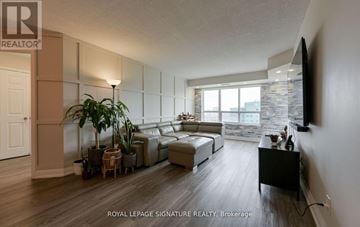 Mississauga (Hurontario) condo for rent - A living room with a couch, a chair, a potted plant, and a television mounted on the wall.