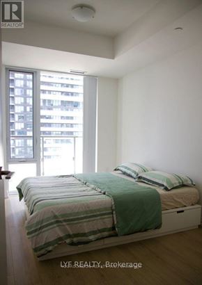Toronto (Waterfront Communities) condo for rent - A bedroom with a bed and a window overlooking a cityscape.