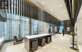 Mississauga (Hurontario) condo for rent - A modern office lobby with a reception desk and a person walking in the background.