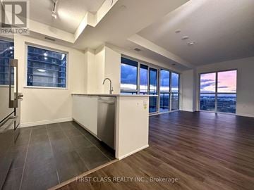 Mississauga (Hurontario) condo for rent - A kitchen with a dishwasher and a refrigerator in a room with wooden floors and a large window.