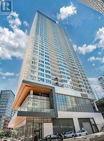 Toronto (Waterfront Communities) condo for rent - A tall building with a glass facade and a wooden top is surrounded by a clear sky.