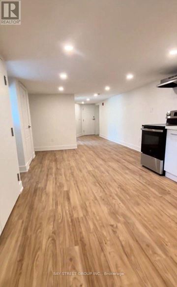 Toronto (East York) multi-family for rent - A spacious room with wooden flooring and a kitchen area with a stove and oven.