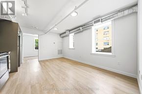 Hamilton (Corktown) multi-family for rent - A spacious room with wooden flooring and white walls.
