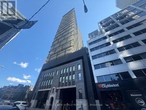 Toronto (Waterfront Communities) condo for rent - A tall building with a glass facade stands next to a smaller building with a stone facade.