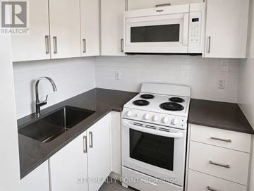 Toronto (Leaside) condo for rent - A white stove and microwave in a kitchen with white cabinets.