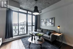 Toronto (Little Portugal) condo for rent - A living room with a grey couch, a coffee table, and a large window with a view of the city.