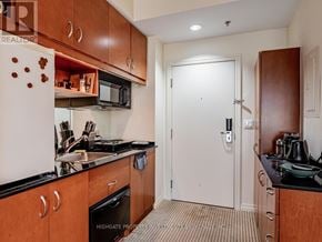 Toronto (Bay Street Corridor) condo for rent - A kitchen with a white refrigerator, brown cabinets, and a black countertop.