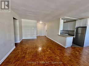 London East (East B) condo for rent - A room with wooden flooring and a kitchen area with white cabinets and a stainless steel refrigerator.