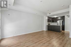 Toronto (Long Branch) townhouse for rent - A spacious room with wooden flooring and a kitchenette in the background.