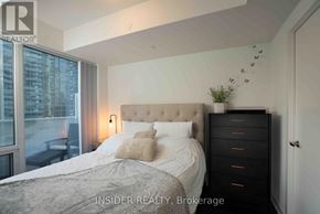 Toronto (Waterfront Communities) condo for rent - A bedroom with a large bed, a nightstand, and a window with a view of a city.