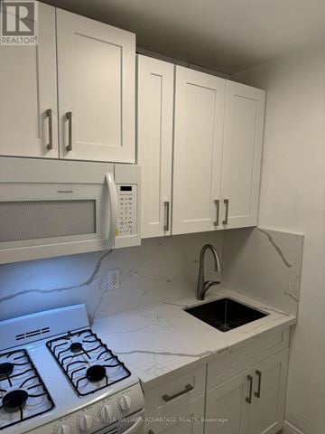 Toronto (Casa Loma) multi-family for rent - A white kitchen with a stove top oven and a microwave above it.