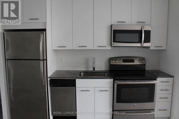 Toronto (Woodbine Corridor) condo for rent - A kitchen with white cabinets and black countertops.