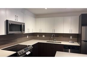 Surrey apartment for rent - A modern kitchen with white cabinets and a black stove top oven.