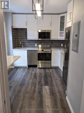 St. Catharines (Downtown) fourplex for rent - A kitchen with white cabinets and a black fridge.