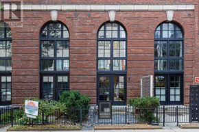 Toronto (Palmerston-Little Italy) condo for rent - A red brick building with arched windows and a black fence in front.