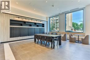Hamilton condo for rent - A modern office space with a long table and chairs, a large window, and a wooden cabinet with drawers.