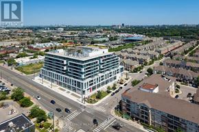 Toronto (Clairlea-Birchmount) condo for rent - A modern multi-story building is situated in the middle of a busy intersection with a clear blue sky above.