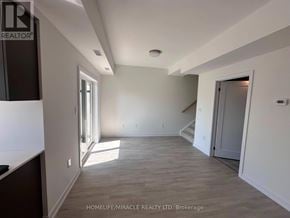 Guelph (Clairfields/Hanlon Business Park) townhouse for rent - A spacious room with wooden flooring and white walls, with a staircase leading to another level.