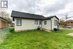 Kitchener apartment for rent - A small house with a white siding and a black roof is surrounded by a green lawn.