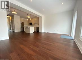 Beamsville townhouse for rent - A large empty room with wooden floors and a kitchen area in the background.