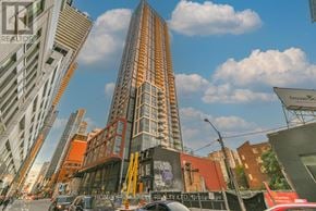 Toronto (Waterfront Communities) condo for rent - A tall building with a glass facade stands in the middle of a city street.
