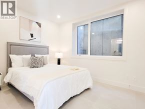 West Vancouver apartment for rent - A bedroom with a large bed, a headboard, a nightstand, a lamp, a window, and a painting on the wall.