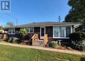 Fort Erie (Ridgeway) apartment for rent - A house with a brown roof and a white door is surrounded by greenery.