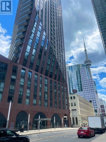 Toronto (Waterfront Communities) condo for rent - A tall building with a glass facade stands next to a shorter building with a red brick facade.