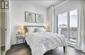 Toronto (Yonge-St. Clair) condo for rent - A bedroom with a large bed and a window overlooking a cityscape.