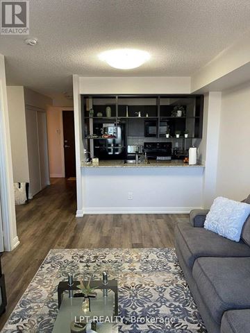 Toronto (Agincourt South-Malvern West) condo for rent - A living room with a grey couch and a coffee table in front of a kitchen area.