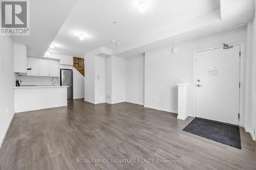 Pickering (Duffin Heights) townhouse for rent - A spacious room with wooden flooring and white walls, featuring a kitchen area with white cabinets and a countertop.