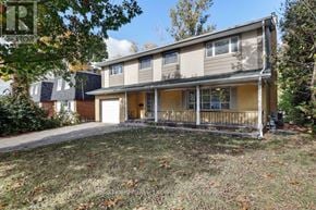 Ottawa apartment for rent - A two-story house with a garage is surrounded by trees and has a lawn in front.