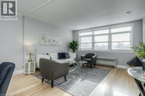 Kitchener apartment for rent - A living room with a grey sofa, a black chair, and a white side table with a lamp.